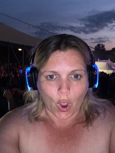 A woman with headphones reacts expressively at an outdoor event during sunset.