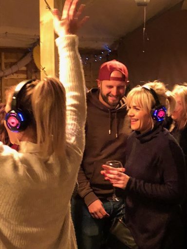 People enjoying a party with glowing headphones and drinks, smiling and socialising.