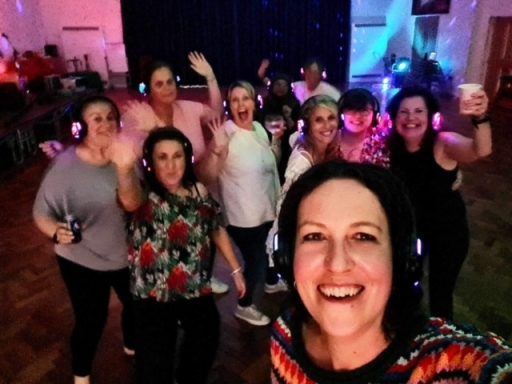 A group of smiling women at a lively event, many wearing headphones and enjoying themselves.