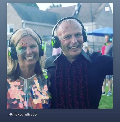 Two smiling people wearing headphones at an outdoor event with festive decorations.
