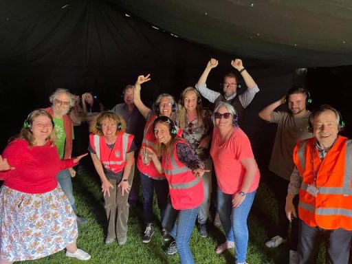 Group of people in casual clothing posing enthusiastically in a dark tent setup.