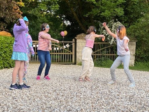 Children playing together outside, dancing and having fun on a gravel surface.