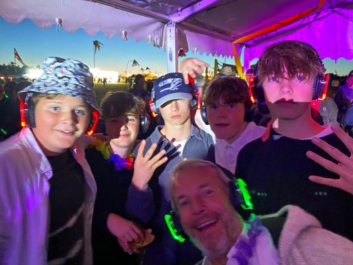 A group of children smiling and posing with headphones at a vibrant outdoor event.